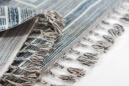 Blue striped woven rug with tasselled fringe, close-up of textured fabric.