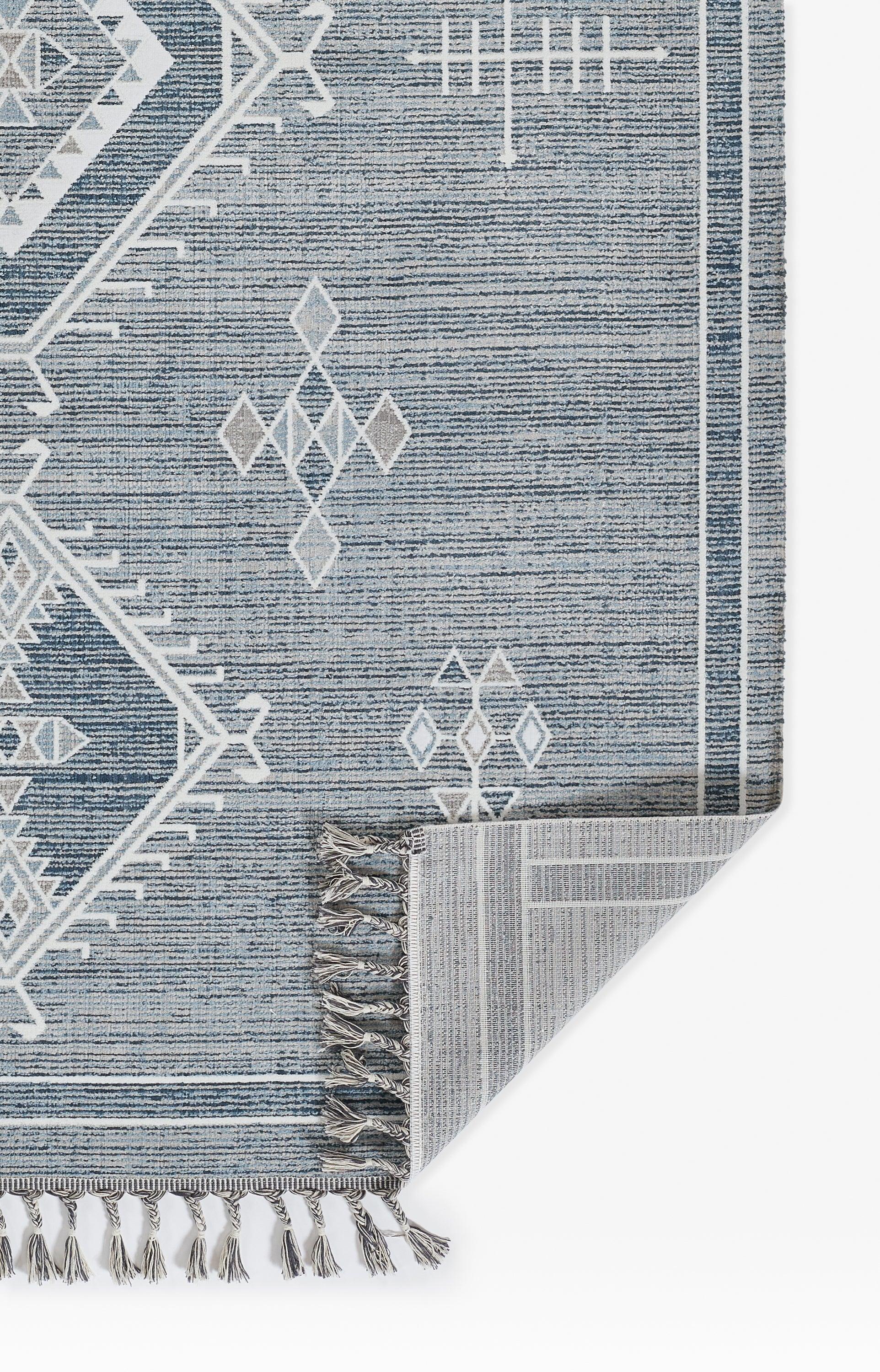 Blue woven rug with white geometric tribal motif, fringed border, rectangular shape, modern boho style.