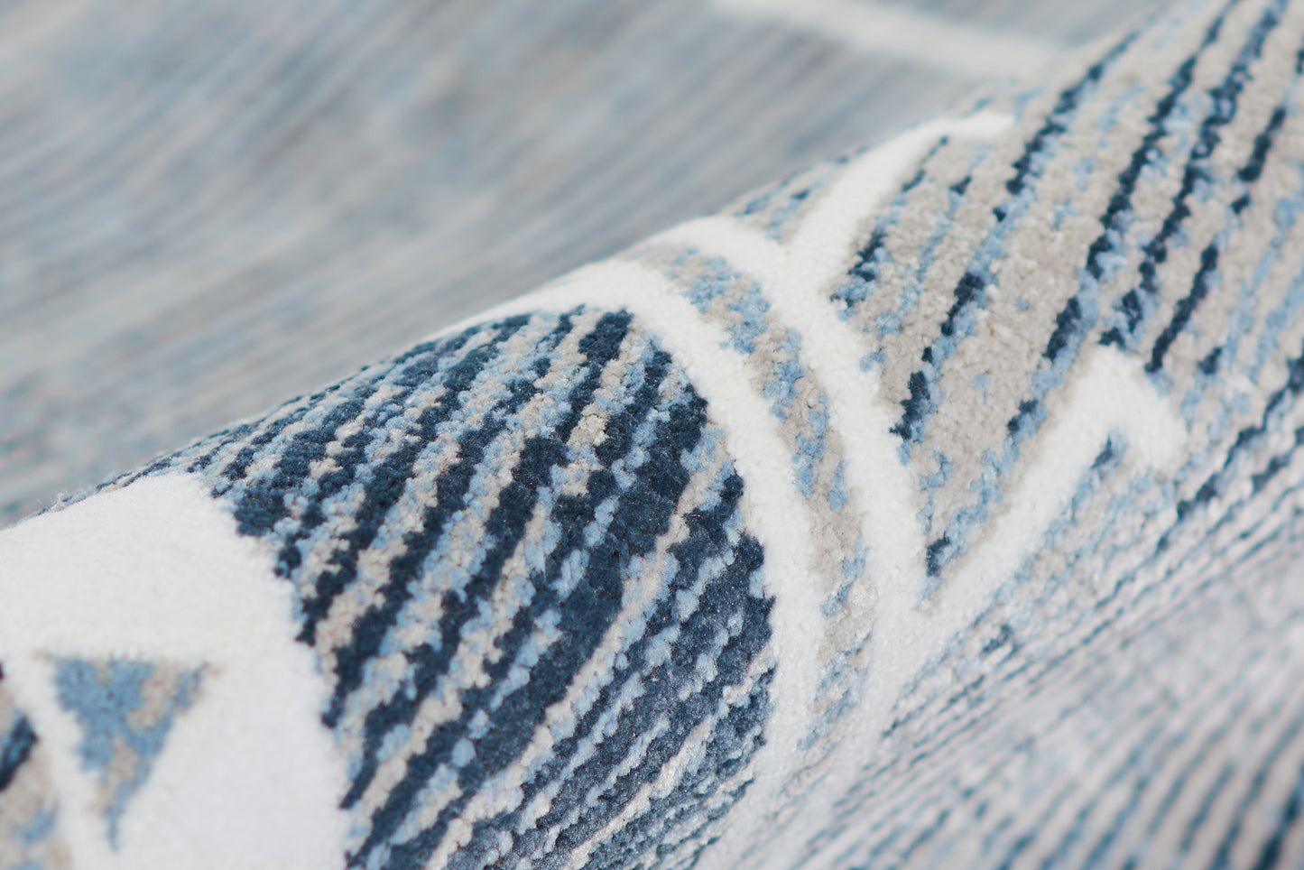 Close-up of a blue and white geometric rug with woven texture and diagonal stripe pattern.