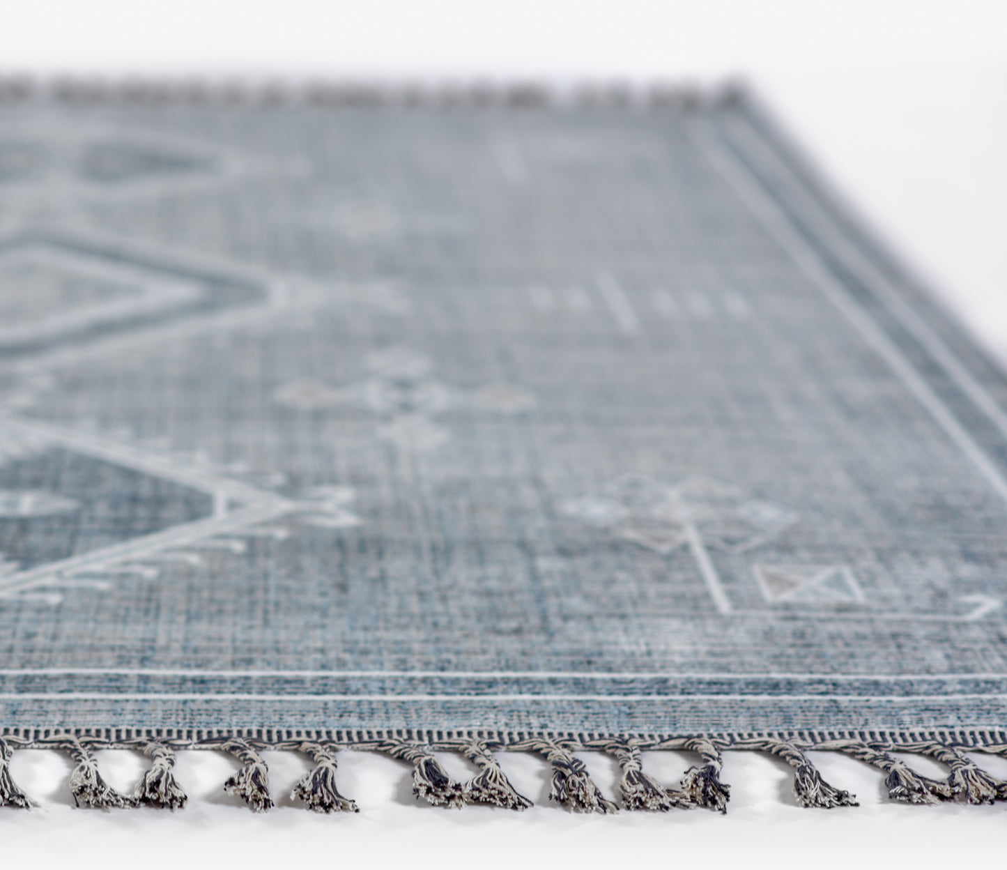 Blue rectangular flatweave rug with white geometric patterns and tassel fringe along the edge.