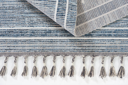 Blue striped rug with twisted fringe tassels along edge and a folded corner revealing textured weave.