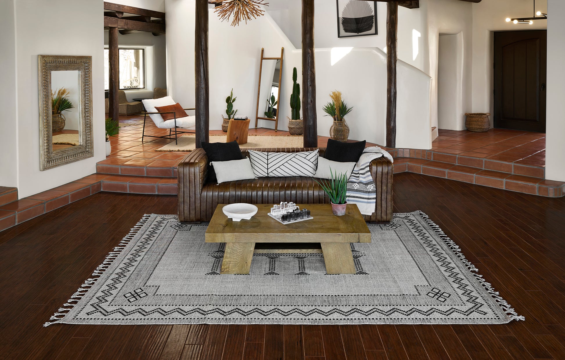 Brown leather tufted sofa with cushions, wooden coffee table on a gray geometric rug in a rustic living room.