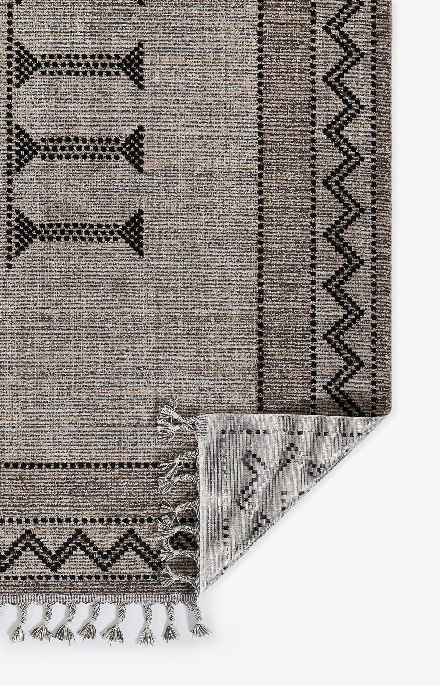 Beige-brown woven rug with black geometric borders, zigzag trim & tassel fringe; folded corner reveals gray underside.