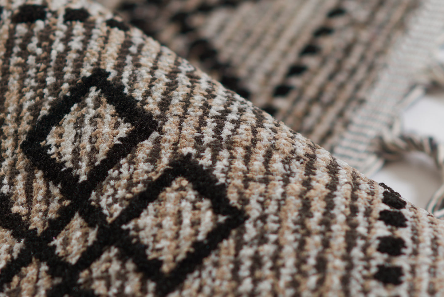 Woven rug in black and tan with geometric diamond pattern and fringed edges, 5' x 8'.