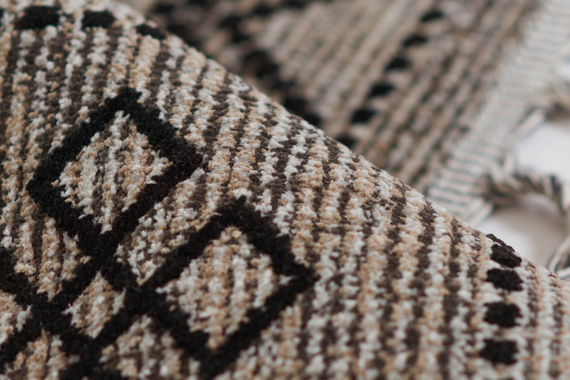 Woven rug in black and tan with geometric diamond pattern and fringed edges, 5' x 8'.