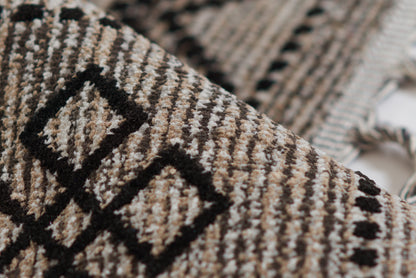 Woven rug in black and tan with geometric diamond pattern and fringed edges, 5' x 8'.