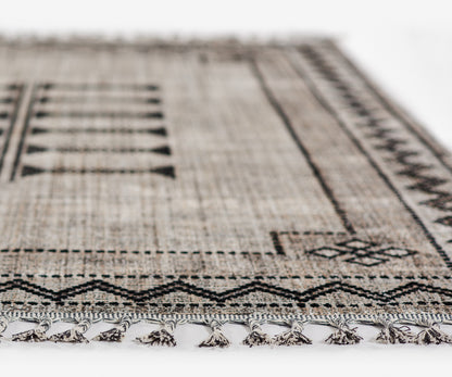 Beige-brown woven rug with a black geometric tribal pattern and fringed tassels along the edge.