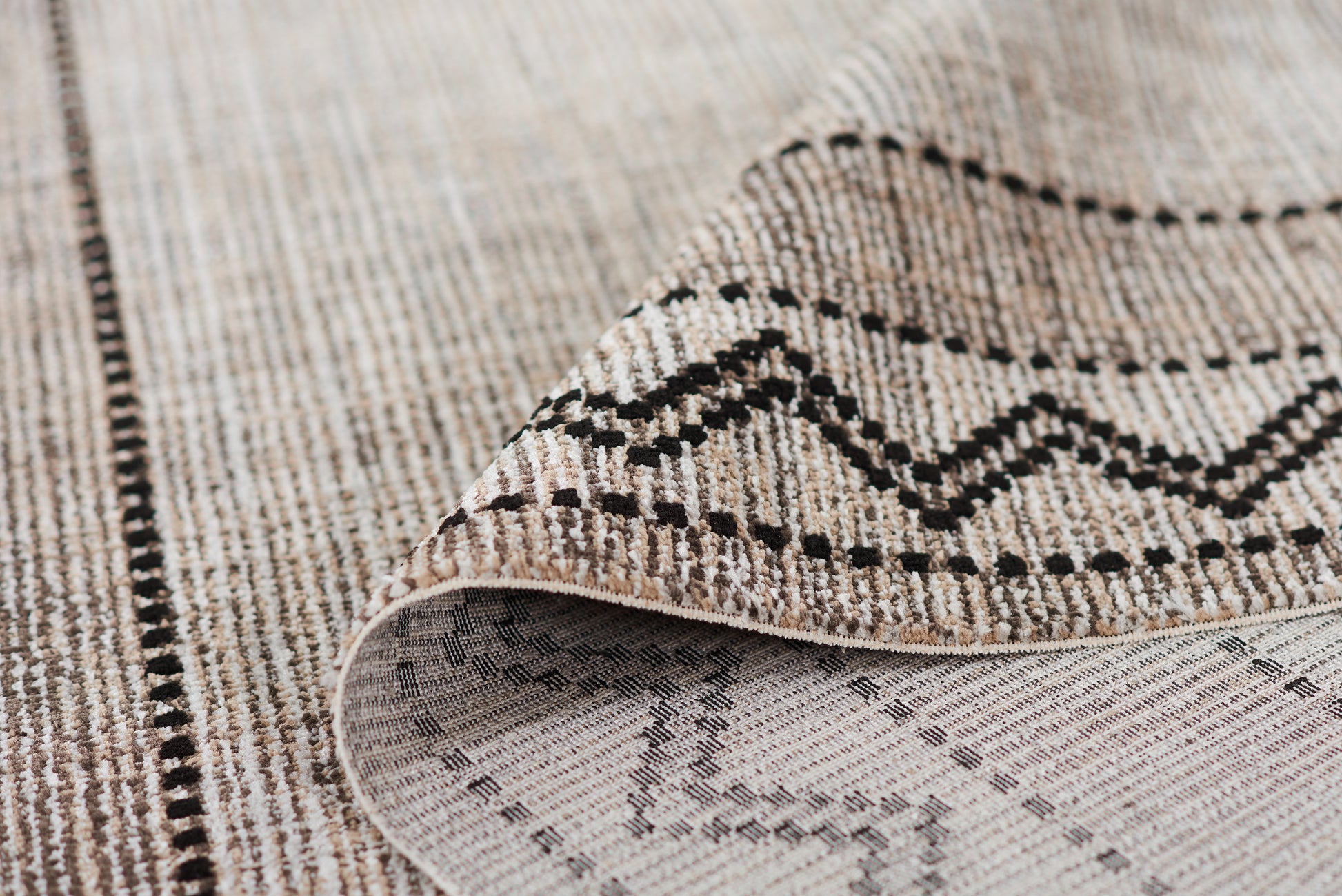 Beige woven area rug with black geometric zigzag pattern and dotted borders; tribal style floor decor.