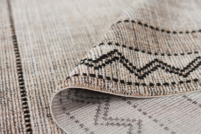 Beige woven area rug with black geometric zigzag pattern and dotted borders; tribal style floor decor.