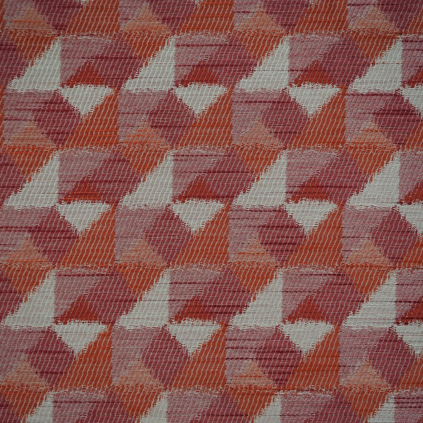Woven fabric with a repeating geometric triangle pattern in burgundy, red, creme, beige, orange, rust and pink.