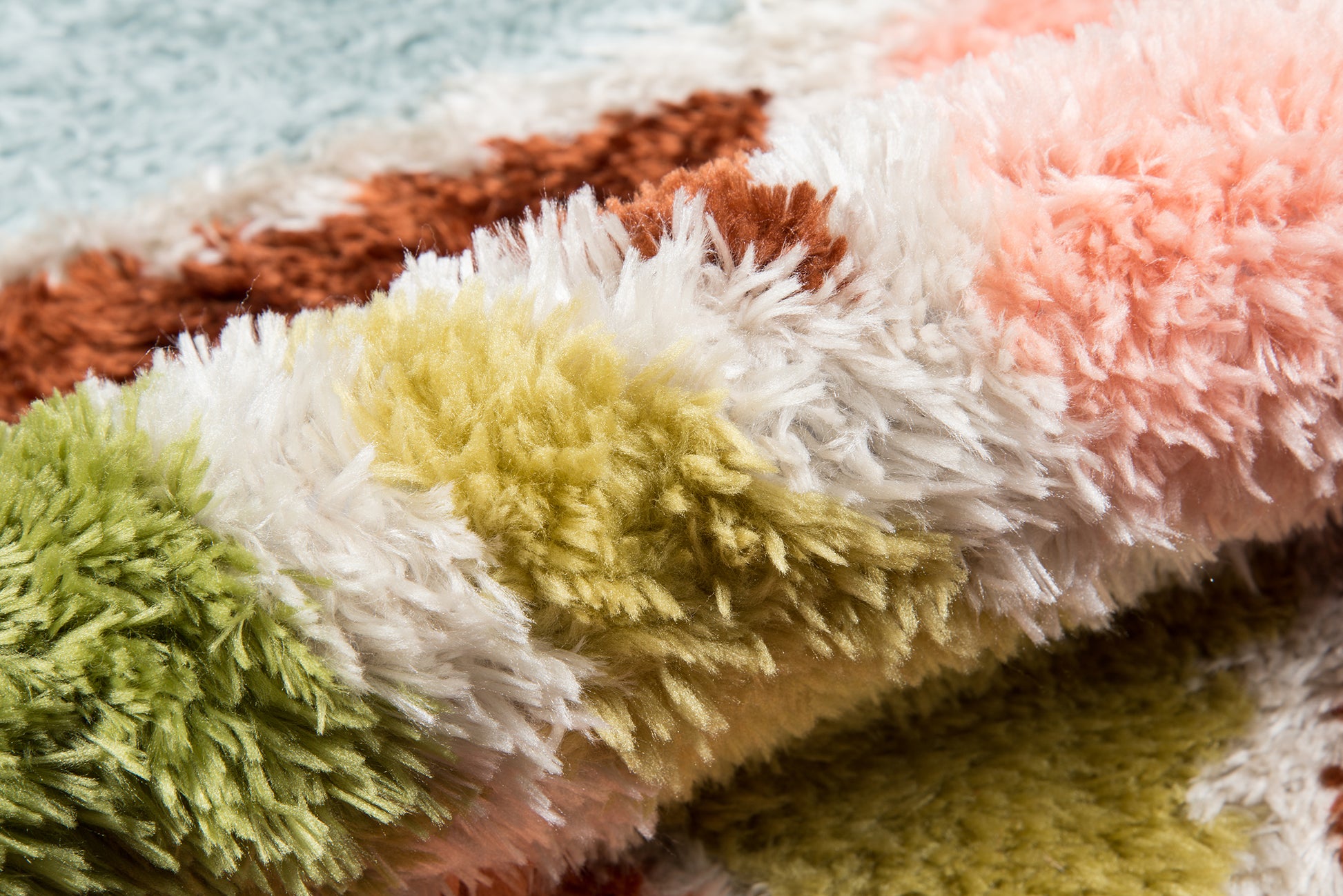 Close-up of a rolled multicolor shag rug with long fluffy fibers in green, white, yellow, brown, and peach.