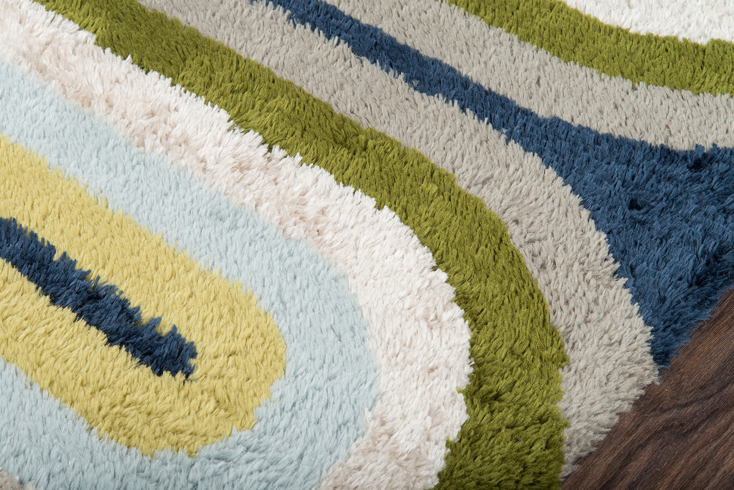 Shag rug with retro multicolor concentric pattern: pale blue, yellow, cream, olive green, gray and navy on a wood floor.