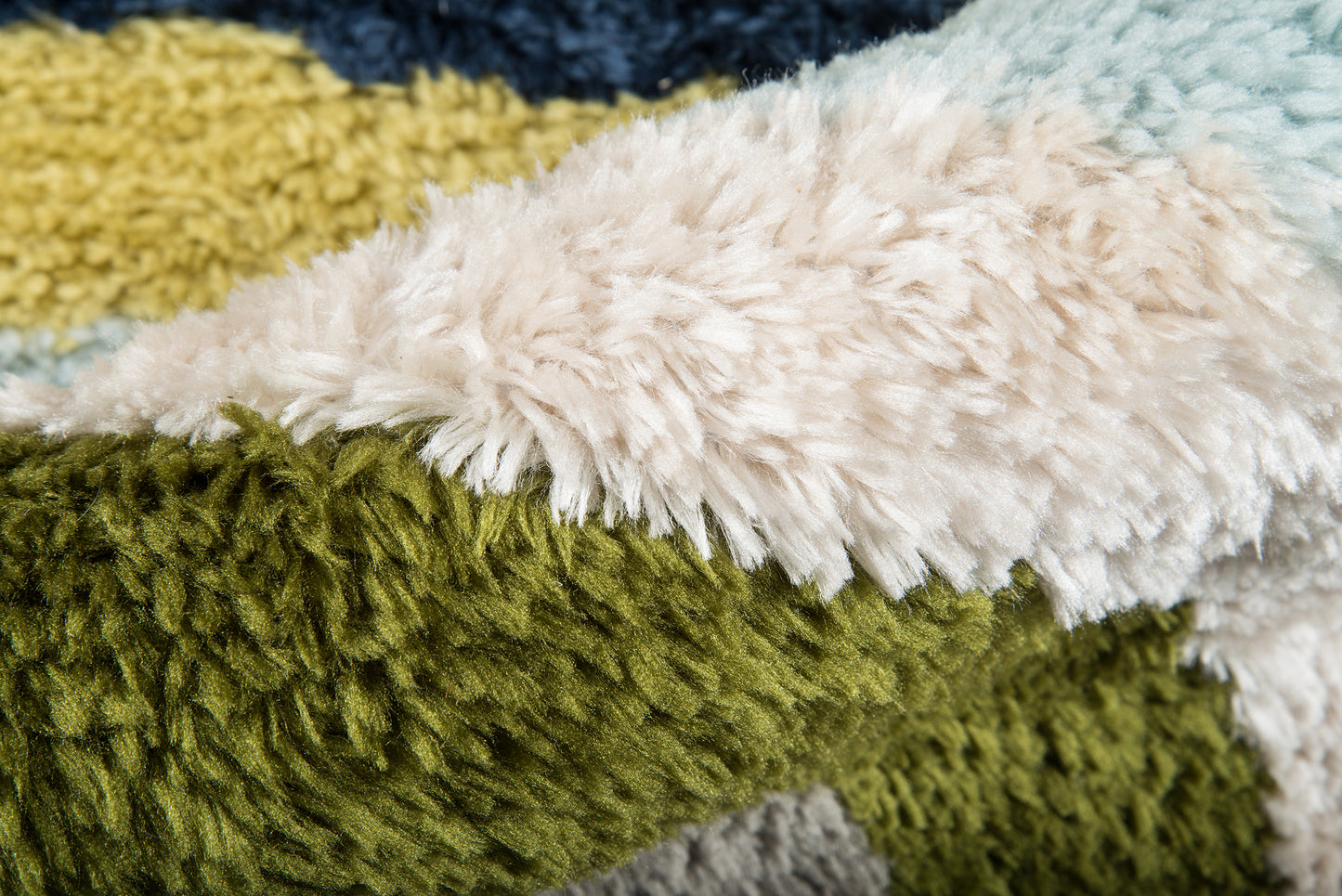 Close-up of a retro-style shag rug with plush strands in olive green, cream, mustard yellow, and blue.