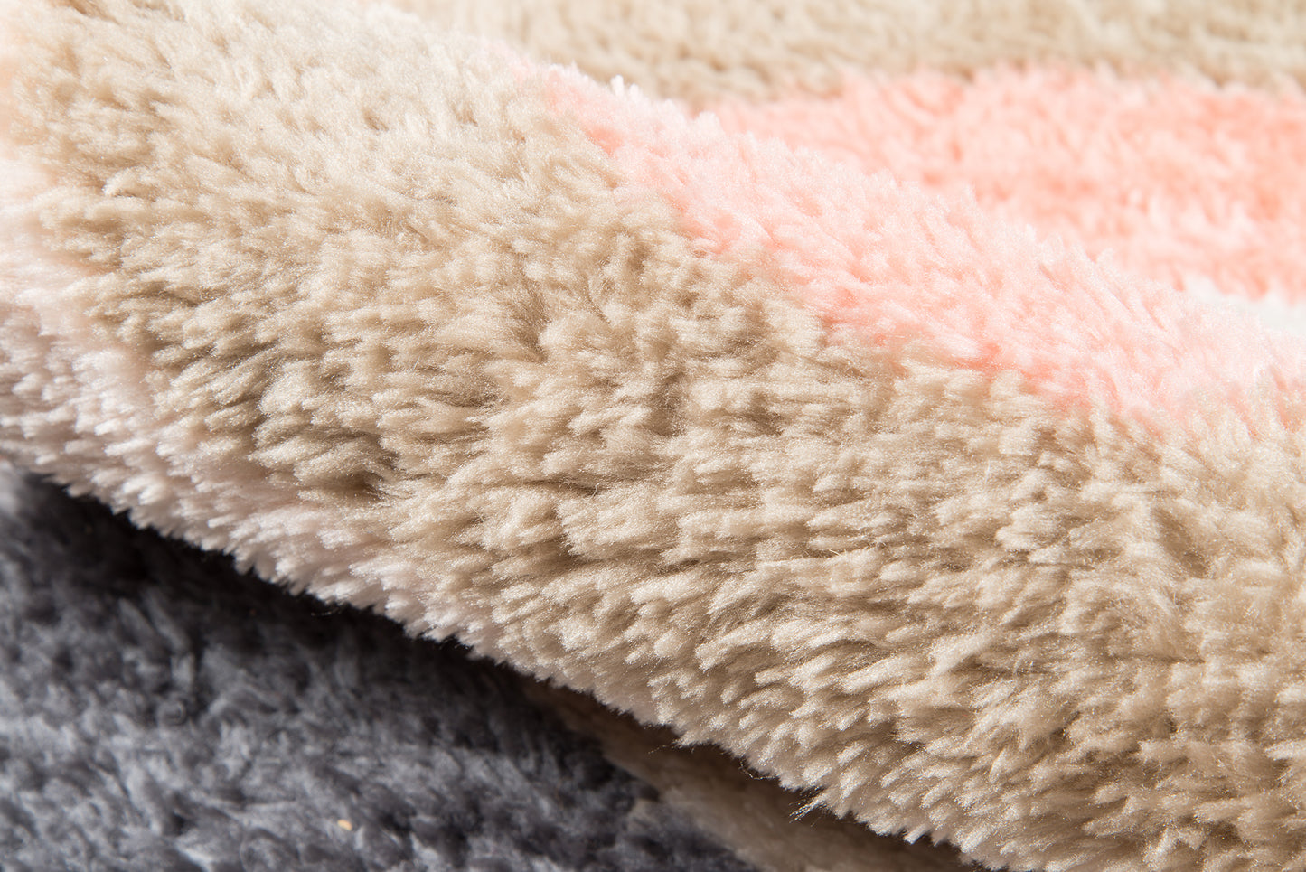 Close-up of shaggy plush rug/throw in beige with a pale pink stripe and dark gray edge.
