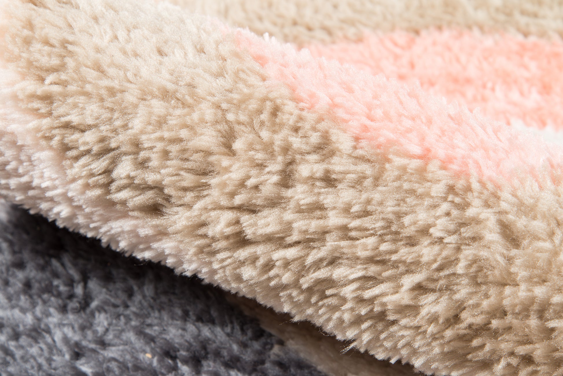 Close-up of shaggy plush rug/throw in beige with a pale pink stripe and dark gray edge.