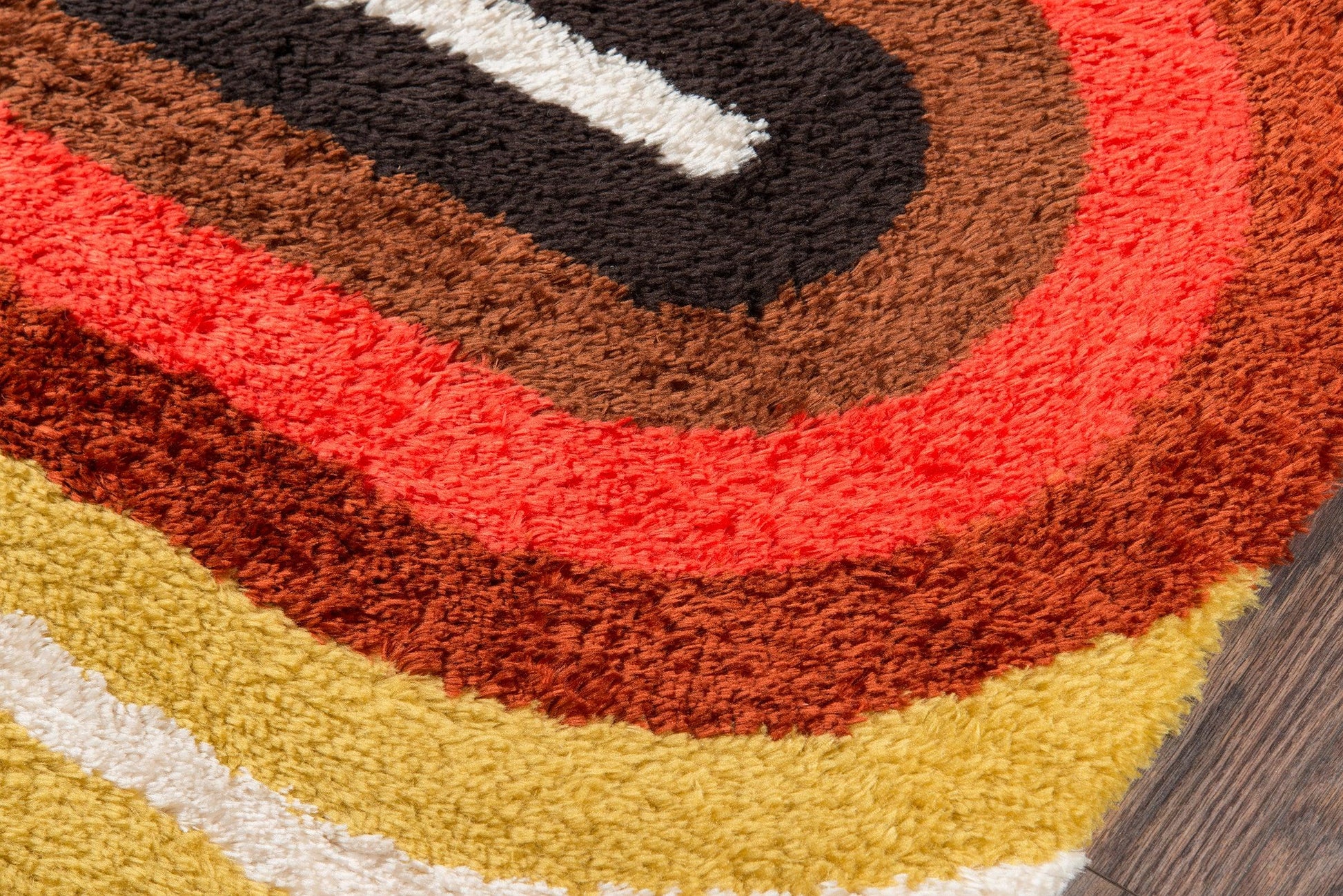 Shaggy rectangular 2' x 8' runner rug with retro multicolor concentric rings in yellow, white, tan, brown, orange, red, and black on wood floor.