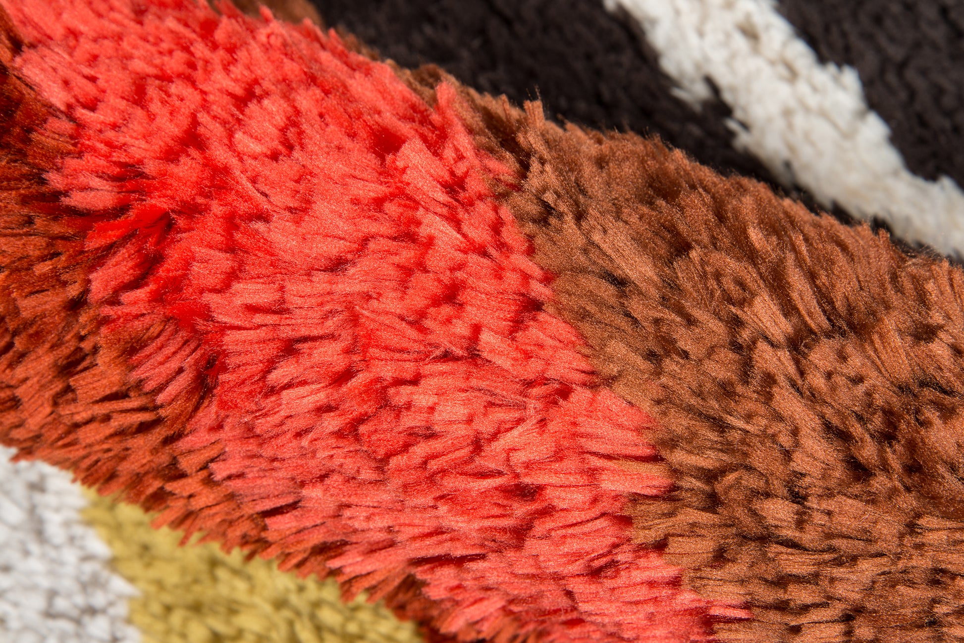 Close-up of a retro shag rug with red and brown plush fibers, thick pile, multicolor stripes for cozy floor decor.