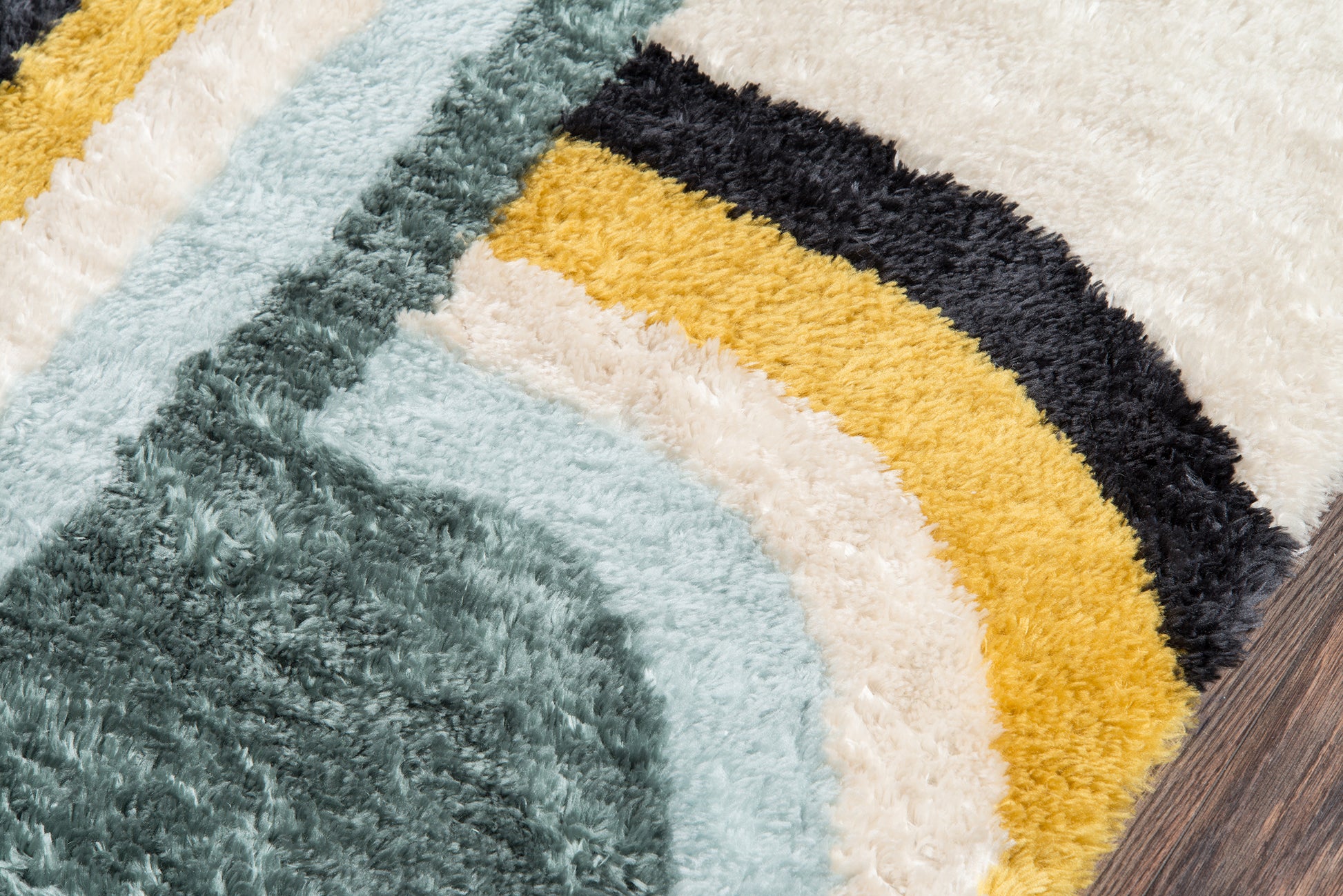 Close-up of a multicolor retro shag rug with teal, light blue, cream, mustard and black curved stripes on wood floor.