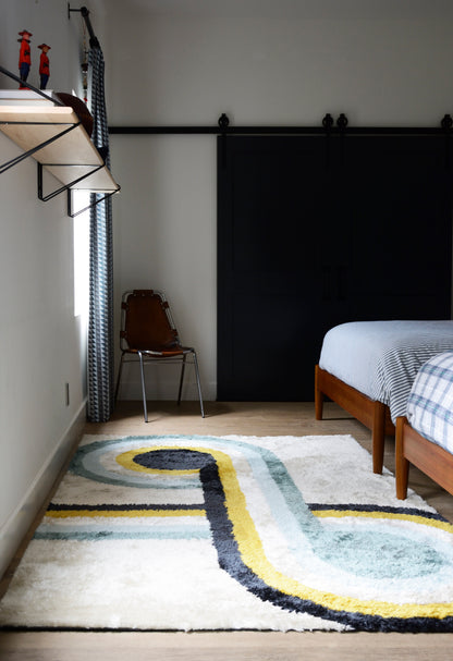 Bedroom with twin wooden beds, blue plaid bedding, black sliding wardrobe, metal chair, and a curved multicolor rug.