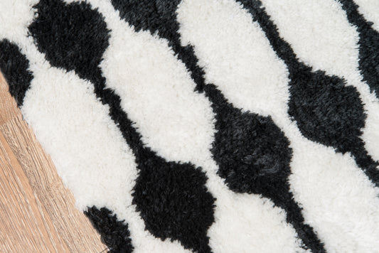 Black and white shag rug with irregular oval shapes on light wood floor.