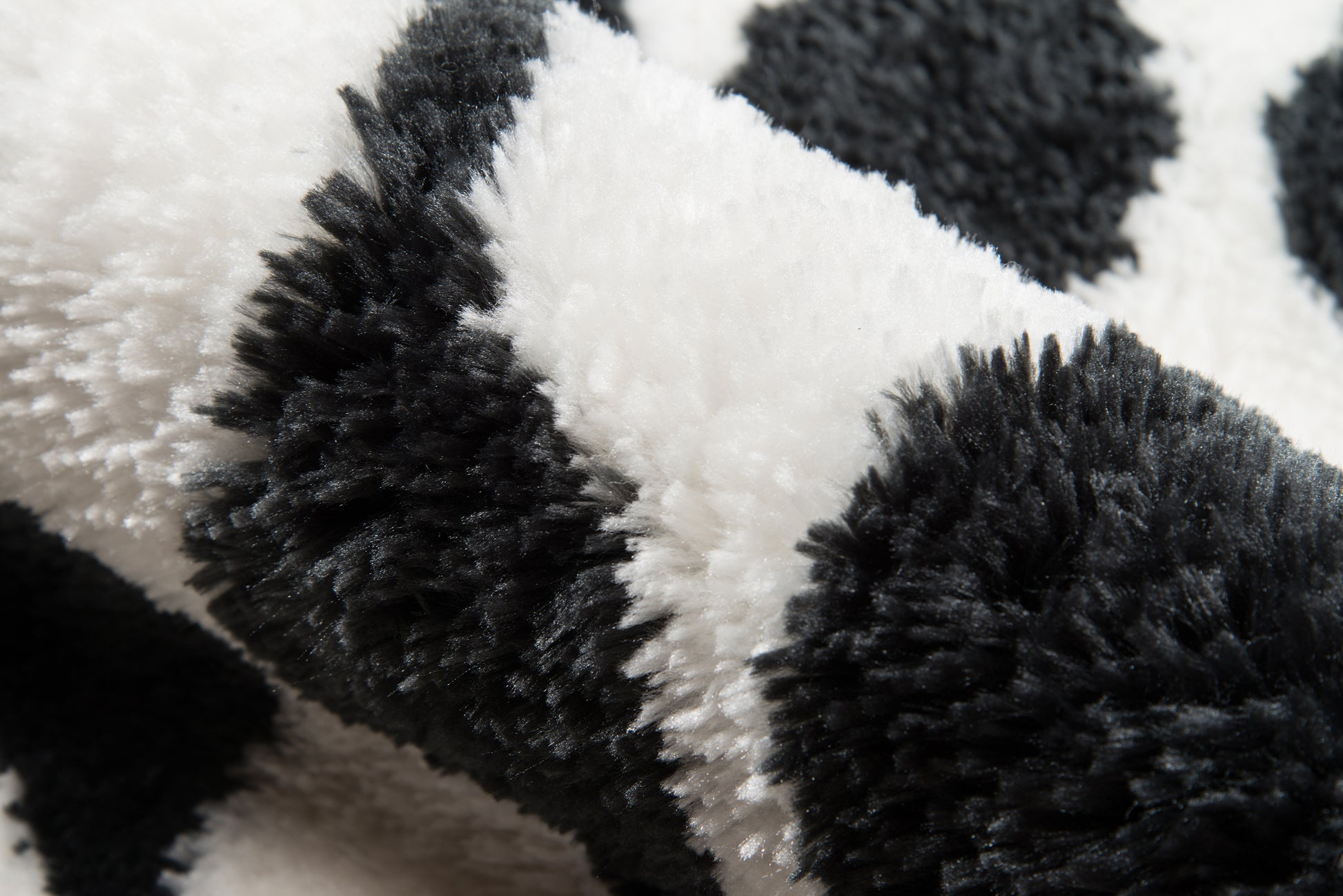 Close-up of black and white shaggy faux fur fabric in a checkerboard pattern; cozy throw blanket or rug.