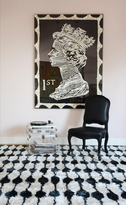 Monochrome retro portrait of Queen Elizabeth II in profile inside a scalloped white frame on a black-and-white rug.