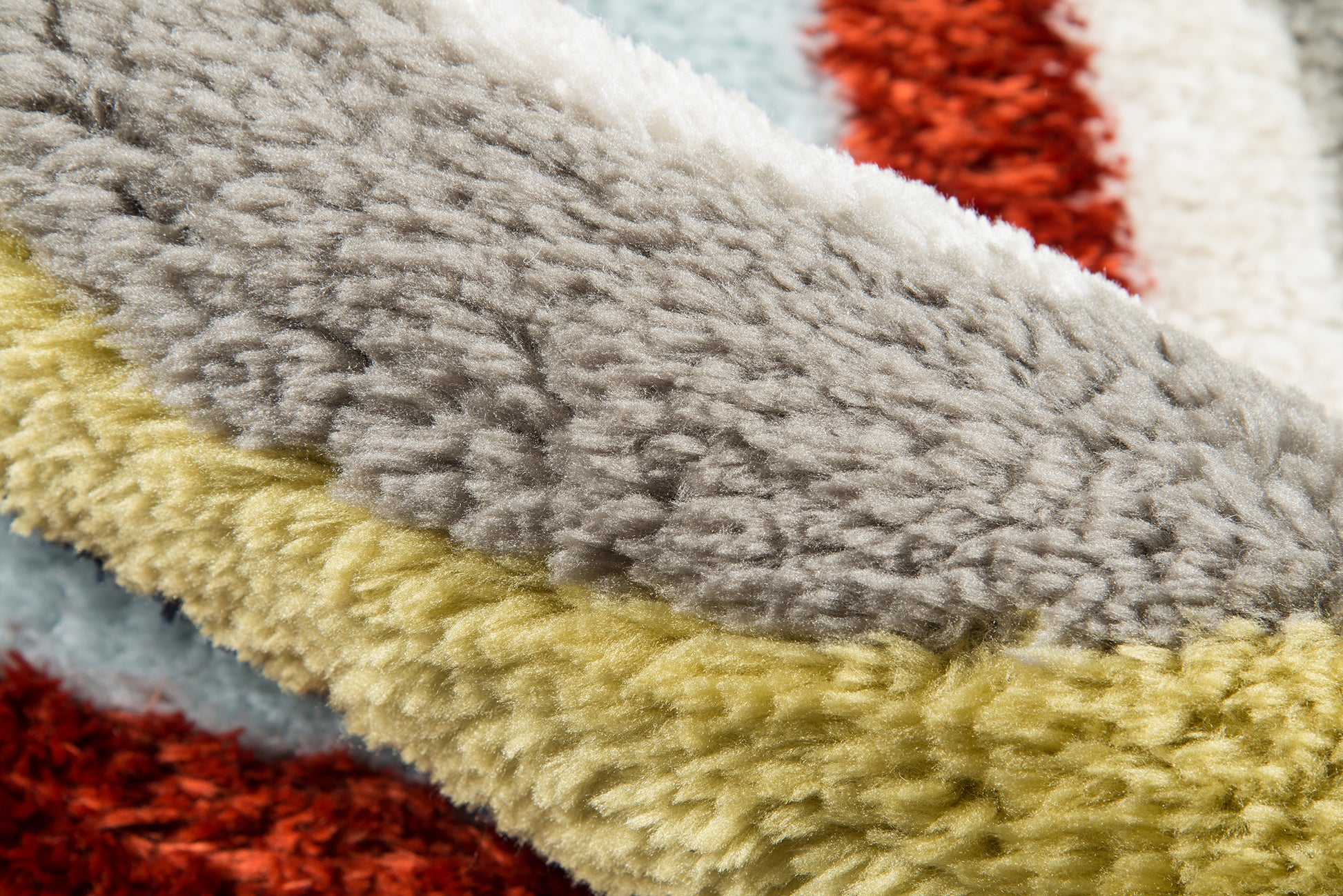 Close-up of a plush shag rug with chunky color bands in gray, cream, mustard, red and pale blue.