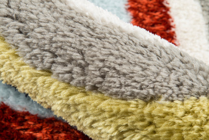 Close-up of multicolor shag rug fibers in gray, yellow, pale blue, cream and red; plush, retro-style texture.