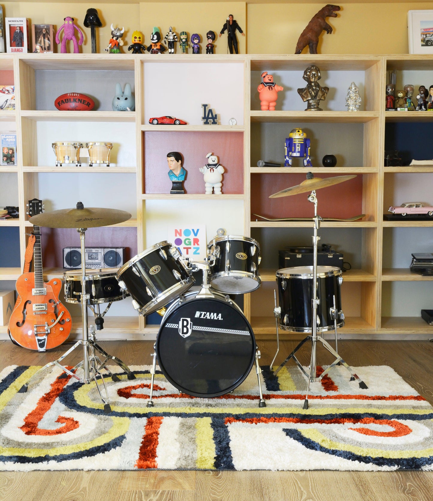 Colorful retro runner rug on the floor; orange guitar on the left and toy shelves in the background.