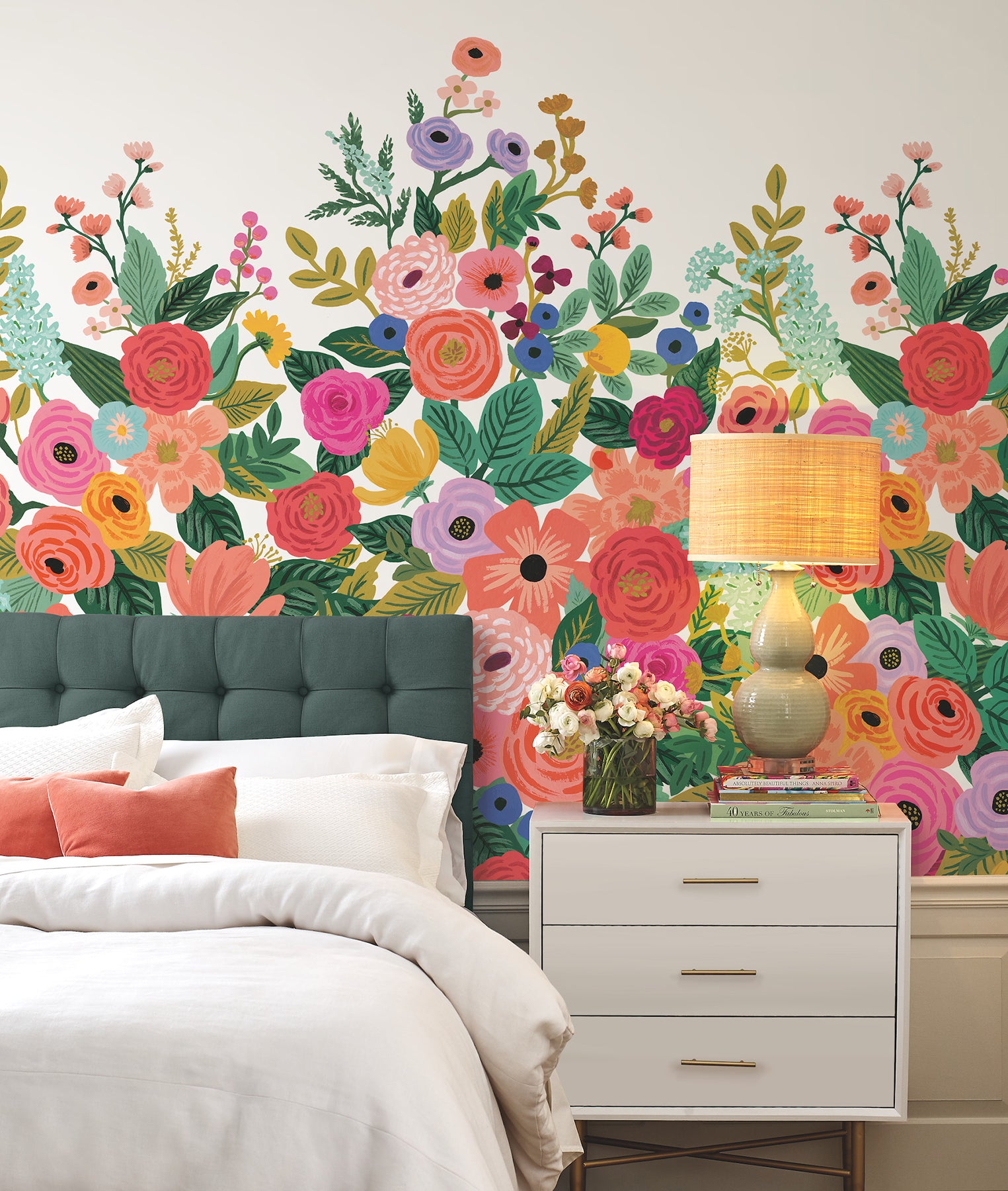 Bedroom with bold floral wall mural, teal tufted headboard, white bedding, peach cushions, and white nightstand with vase.