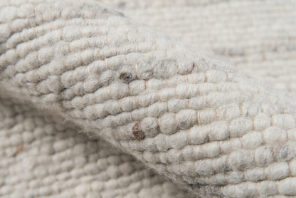 Close-up of a chunky ivory boucle wool rug with thick loop texture.