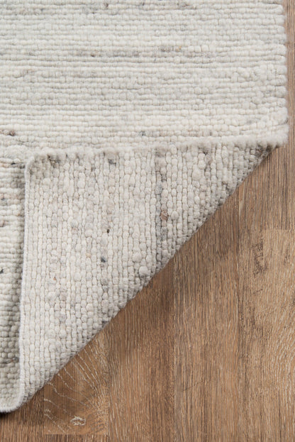 Cream ivory loop-pile rug; folded corner exposes backing on warm wood floor.