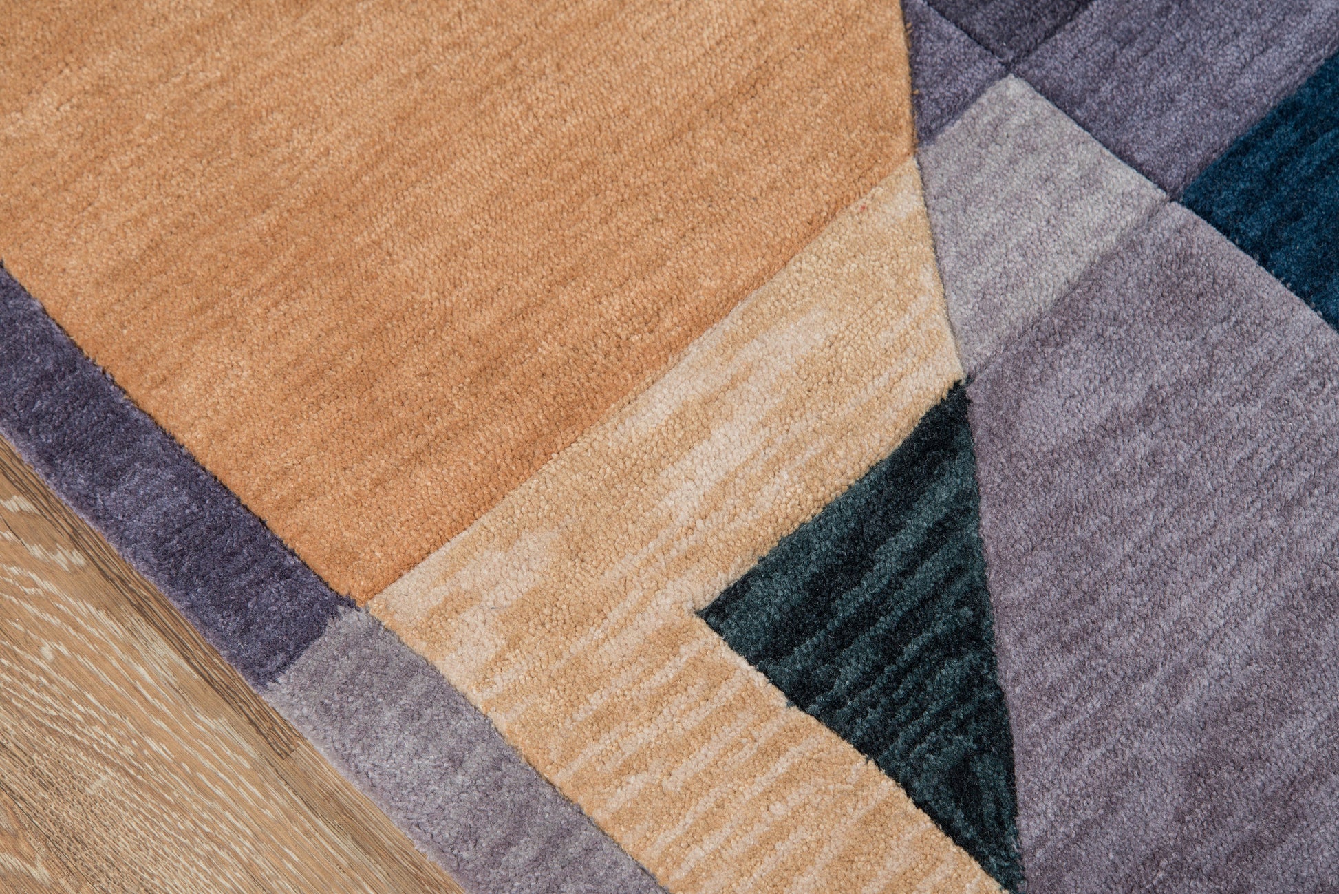 Close-up of a multicolor geometric rug with patchwork triangles in orange, beige, lavender, purple and teal.