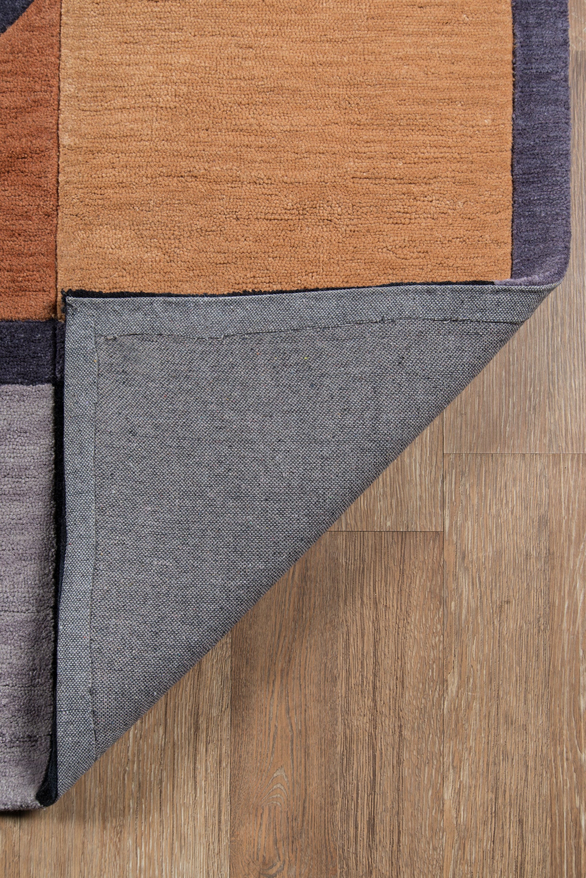 Geometric color-block rug in orange, navy and charcoal; folded corner shows grey underside on wood floor.