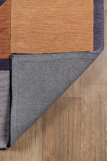 Geometric color-block rug in orange, navy and charcoal; folded corner shows grey underside on wood floor.