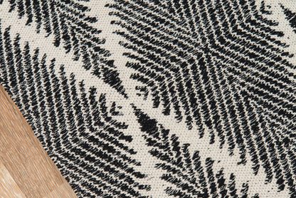 Cream woven rug with black fern-leaf pattern on wooden floor.