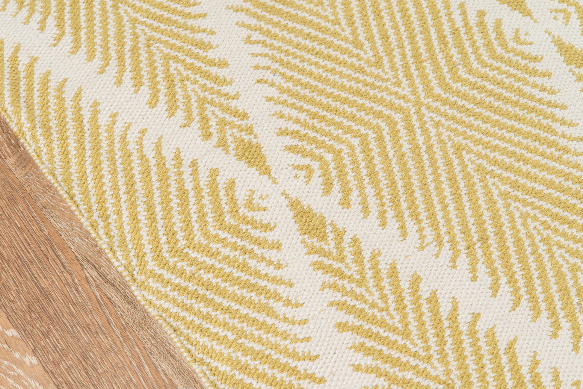 Cream woven rug with yellow fern-like pattern, wood floor edge visible; boho indoor decor rug.