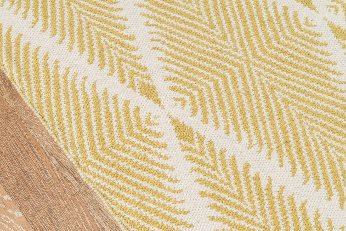 Yellow fern-patterned woven runner rug on beige background with a wood floor edge visible.
