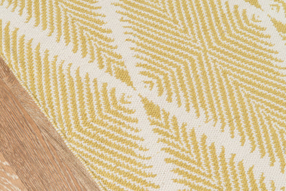 Yellow fern-patterned woven runner rug on beige background with a wood floor edge visible.