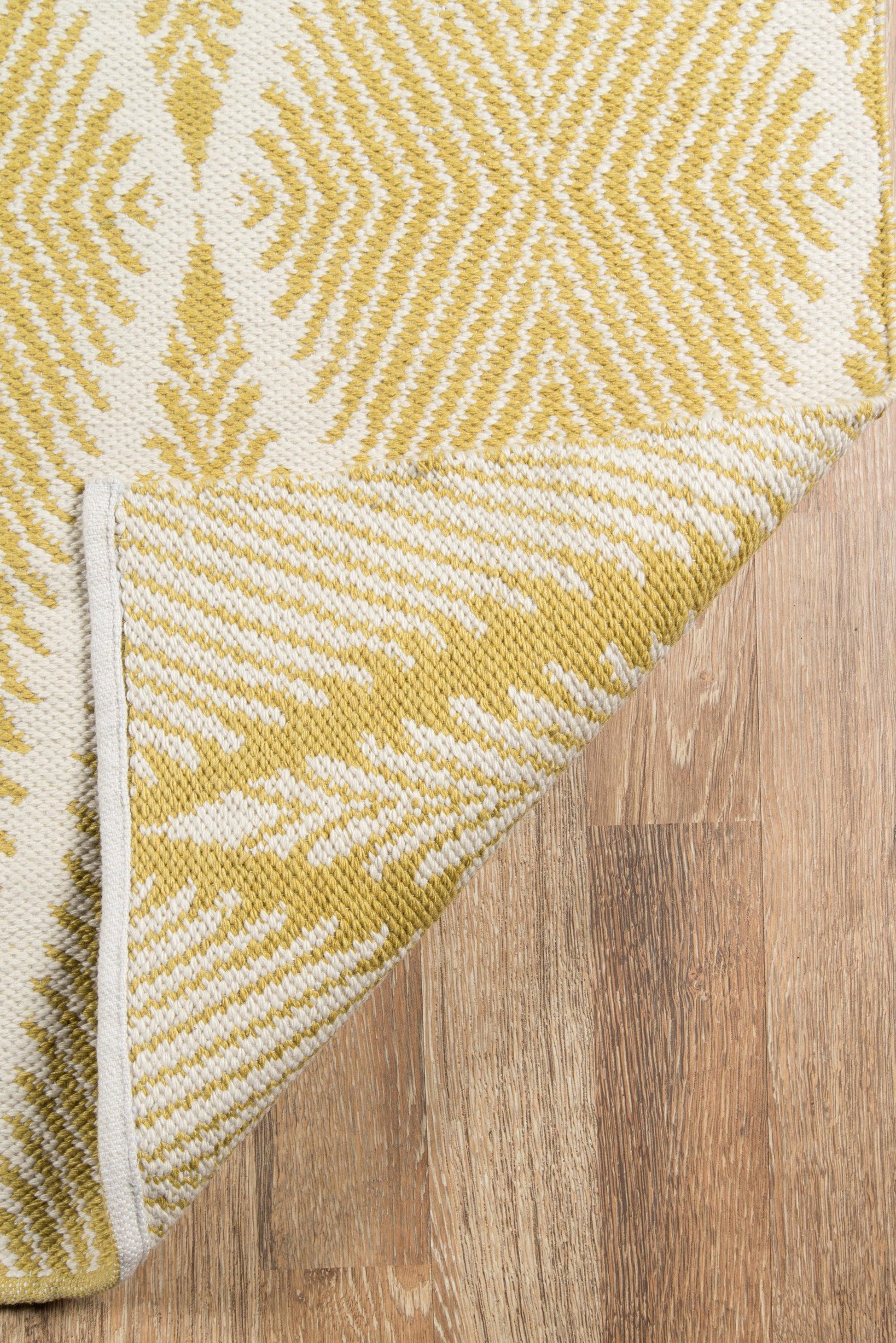 Yellow and white geometric woven rug with a starburst pattern, folded corner on a wood floor.