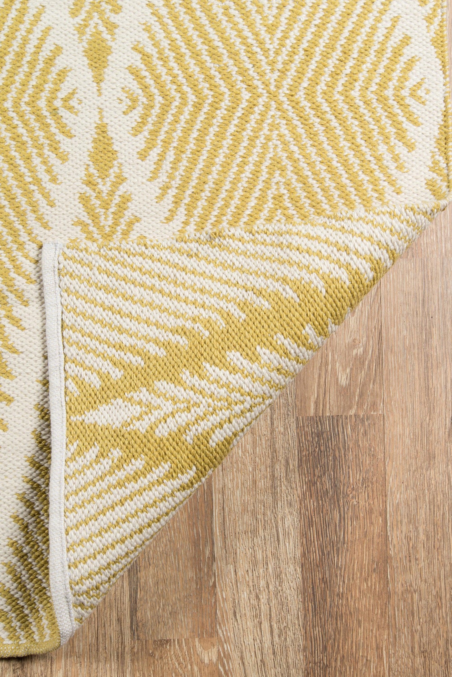 Mustard yellow and ivory geometric woven rug on wood floor, folded corner reveals white edging.