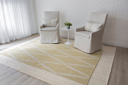 Two beige slipcovered armchairs with a white round side table on a pale yellow geometric rug in a bright minimal living room.