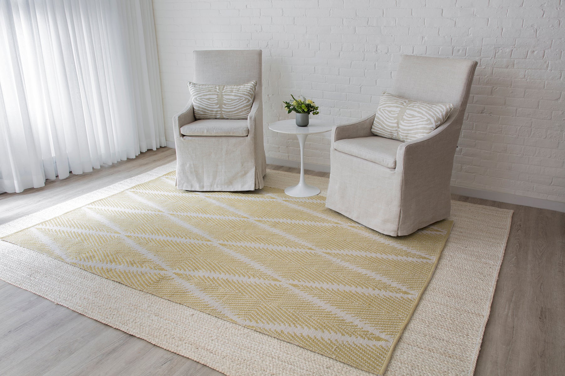 Beige slipcovered armchairs with a white pedestal table between, set on layered yellow geometric and beige area rugs.