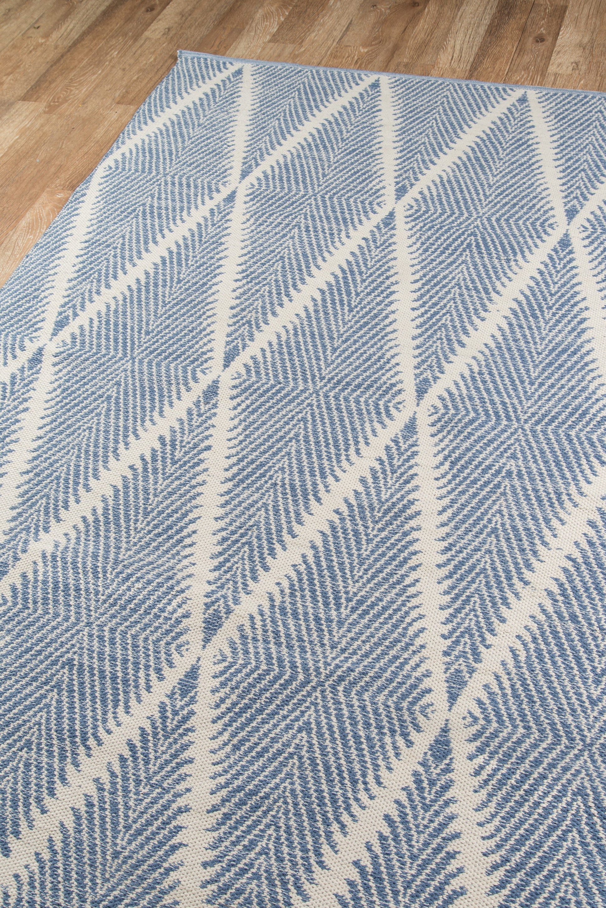 Blue and white woven rectangular rug with diagonal chevron pattern on a wood floor.