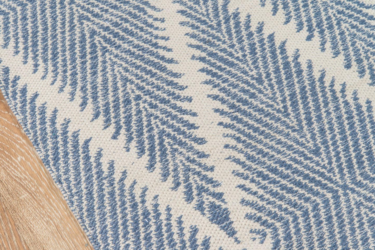 Blue fern-patterned beige woven rug on wood floor; coastal, textured textile.