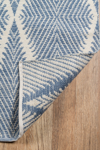 Blue and cream woven rug with river motif and diamond zigzag pattern, folded corner on wood floor.
