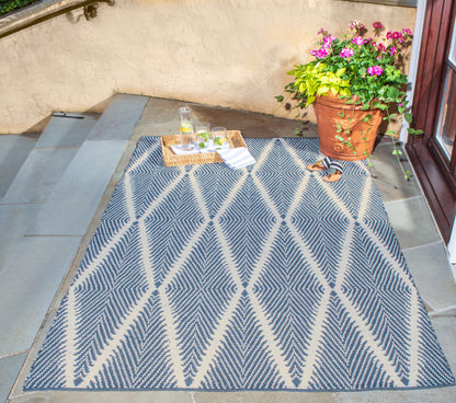 Outdoor rug with navy and cream diamond pattern on stone steps; tray of drinks, sandals and a potted flowering plant nearby.