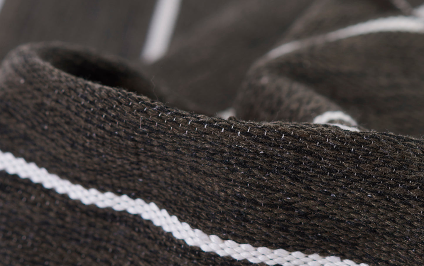 Close-up of a dark brown rug with a white stripe, showing textured weave and stitch detail.