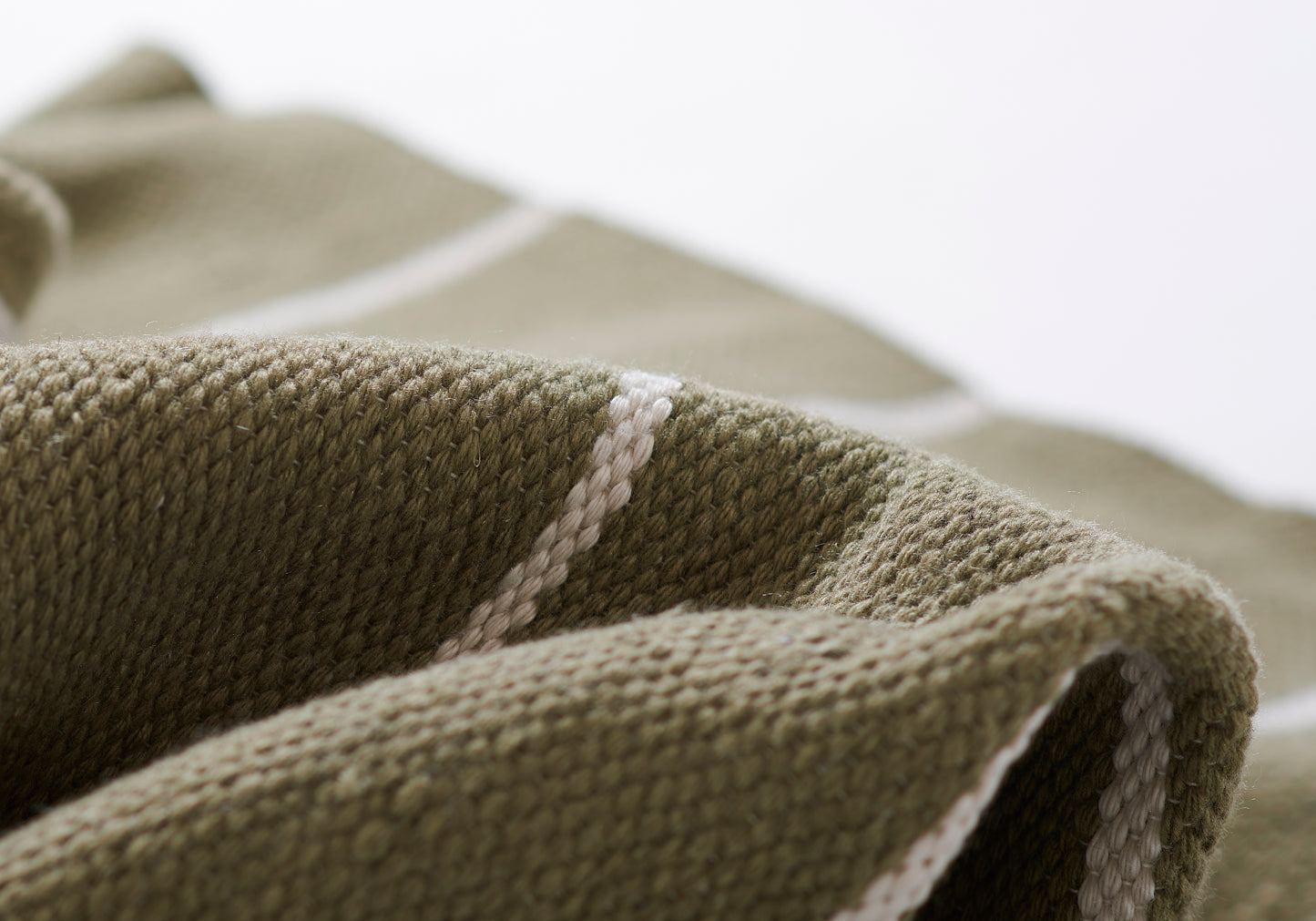Close-up of an olive-green rug with a white stripe edge; soft woven texture.