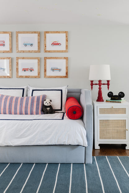 Gray-blue sofa with white cover, striped cushions, panda plush; white side table with woven drawers, red lamp, striped rug.